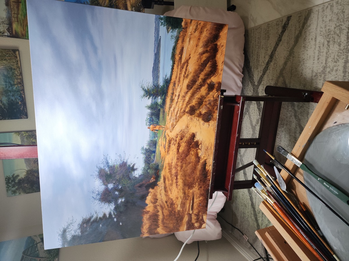 Una pintura de un sendero junto al agua sobre el caballete, con pinceles en el estudio